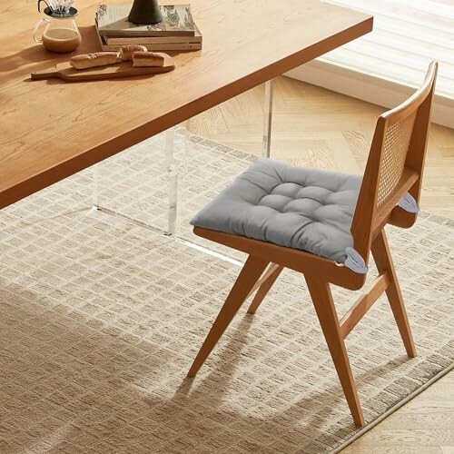 A modern wooden chair with a gray cushion at a wooden table on a textured rug.
